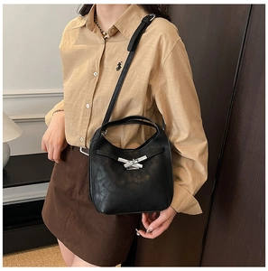 Détail d'un sac seau noir avec fermoir argenté porté en bandoulière par un mannequin