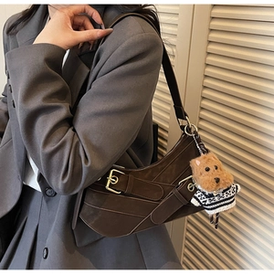 Detail of dark brown suede crescent shoulder bag with metal buckles and dog plush charm