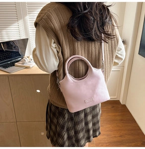 Sac à main rose en similicuir avec poignée arrondie porté par un mannequin en extérieur
