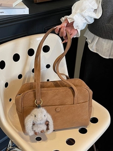 Brown suede bowling bag with shoulder strap and plush rabbit charm on a stylish chair