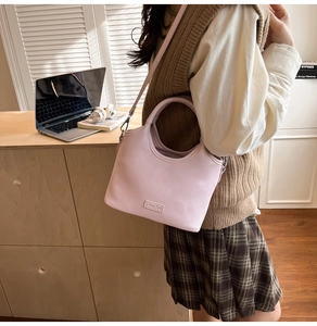 Détail du sac à bandoulière rose pâle avec logo en métal et lanière en décor de bureau