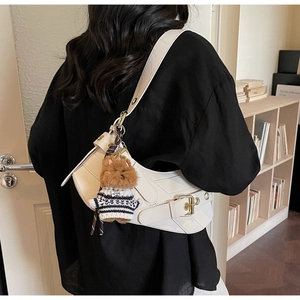Detail of white crescent shoulder bag featuring crossed belts and cute bear plush charm