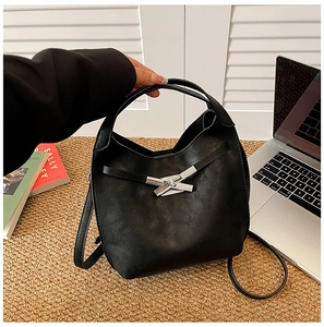 Détail du sac seau en cuir noir avec fermoir en métal argenté sur une surface tissée