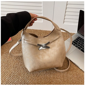 Détail du sac seau texturé beige avec une boucle métallique argentée décorative en croix