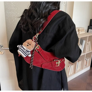Side view of a burgundy suede saddle bag with gold buckles and a brown bear charm