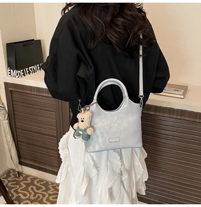 Détail d'un sac à main bleu clair brillant avec breloque d'ours en peluche et logo argenté