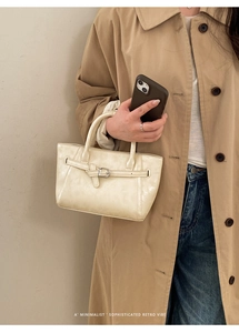 Close-up of minimalist cream white bucket bag featuring elegant metal buckle and twin handles