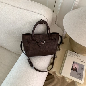 Detail of dark brown matte leather handbag with adjustable strap on a sofa