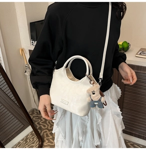Détail d'un sac à main blanc minimaliste en cuir avec un charmant ours en peluche