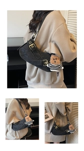 Detail of a vintage black suede saddle bag with golden buckle and a cute bear charm