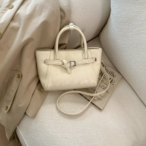 Detail of cream faux leather handbag with belt buckle on a tweed sofa and trench coat