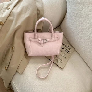 Detailed view of pink leather bucket bag with decorative belt on soft white fleece sofa