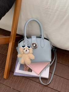 Light blue leather handbag with teddy bear charm and silver lock on a home background