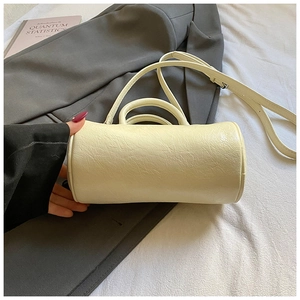 Detail of a creamy off-white cylindrical bag with pleated texture and adjustable strap