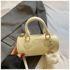 Creamy yellow cylinder handbag placed on a grey blazer with a cute sheep charm