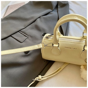 Detail of cream pillow bag with silver zippers, fur ball charm, and long shoulder strap