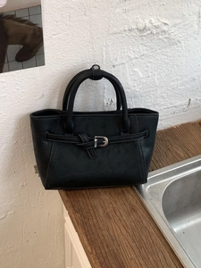 Minimalist black matte leather handbag with buckle detail on a dark wooden countertop