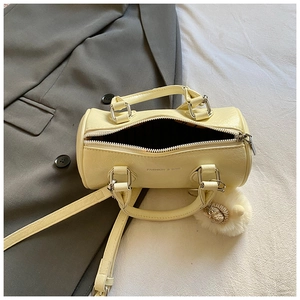 Detail of light yellow cylinder handbag with smooth leather texture and plush pompom charm