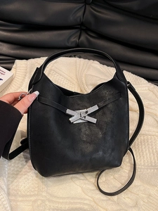 Sac seau chic en simili cuir noir avec fermoir métallique argenté sur un pull en tricot