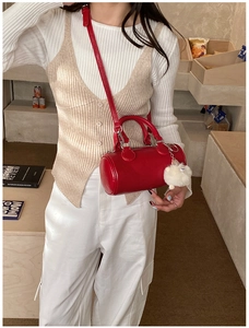 Red cylindrical crossbody bag with white fur charm shown in a cozy lifestyle setting