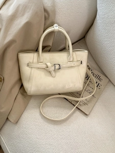 Minimalist cream white top handle satchel bag with retro buckle on a cozy sofa