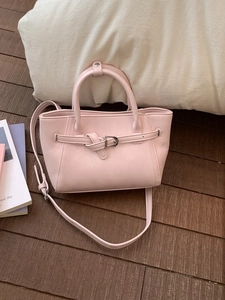 Pale pink leather top-handle crossbody bag with buckle detail on a dark wooden floor