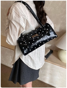 Detailed side view of a black polka dot cylindrical bag with silver metal buckle and strap