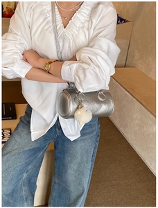Silver cylindrical handbag with plush charm shown with casual lifestyle outfit