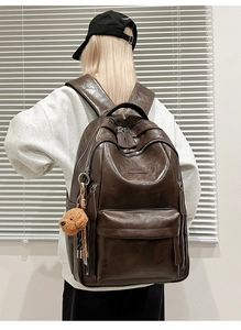 Detail of dark brown leather backpack with plush bear charm and vintage texture