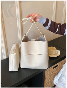 Detail of minimalist cream white bucket bag with matching pouch on a dark wooden table