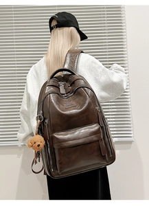 Close-up of vintage brown PU leather backpack with oil-wax texture and plush bear charm