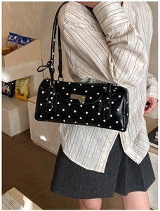 Polka dot cylinder shoulder bag with heart charm and glossy finish worn by model