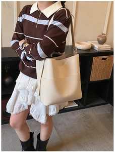 Detail of a beige leather bucket bag with wide shoulder strap worn by a female model