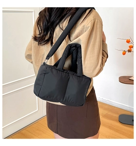 Close-up of black quilted puffer tote bag worn by model in a minimalist modern room