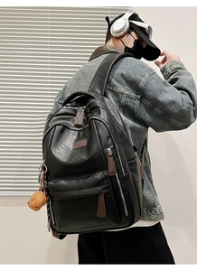 Detail of black matte leather backpack featuring brown zippers and a plush bear keychain