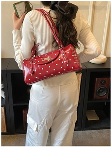 Detail of red polka dot cylinder bag with glossy finish and silver buckle on model