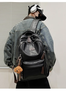 Rear view of a black PU leather large backpack with a plush dog charm on a denim model