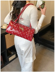 Detailed view of red polka dot shoulder bag featuring a heart pendant and metal accent