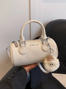 White cylinder pillow bag with plush charm and detachable strap shown in lifestyle view