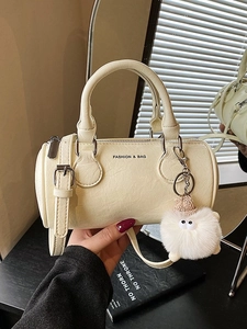 Chic beige leather boston bag with top handles and plush charm in a trendy lifestyle setting