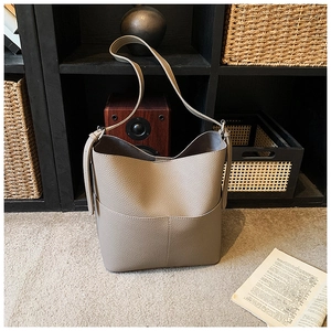 Close-up of a taupe bucket bag with pebbled leather texture on a cozy carpet