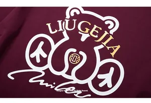 Detail of bear graphic and gold lettering on burgundy oversized t-shirt fabric