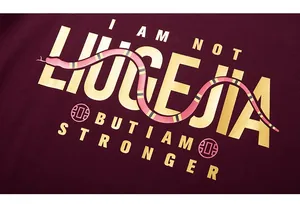 Close-up of golden letter print and snake graphic on burgundy cotton t-shirt fabric