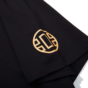 Close-up of black cotton T-shirt sleeve with gold circular logo and double stitching
