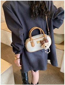 Detail of cream and brown bowling bag with plush bear charm worn by a model