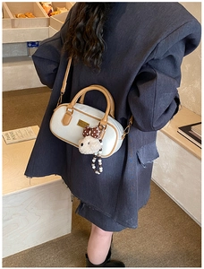 Close-up of white pebble leather bowling bag with teddy bear charm and gold logo
