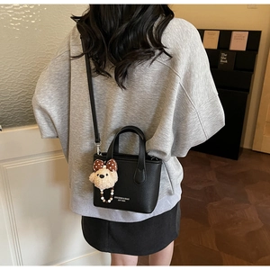 Detail of black pebbled leather mini bucket bag with plush bear charm and crossbody strap