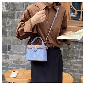 Close-up of blue denim box bag featuring contrast stitching and brown leather handle
