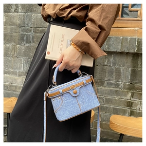 Detail of denim box bag with leather trim and decorative belt in a street setting