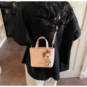 Pink mini bucket bag with teddy bear charm shown cross-body on a model in a cozy interior
